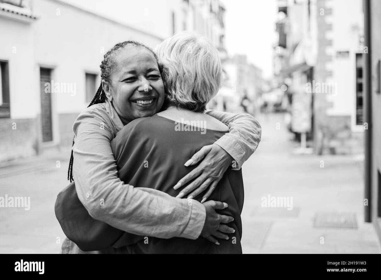 Multiracial senior women hugging each other - Elderly friendship and love concept - Focus on african woman face - Black and white edition Stock Photo