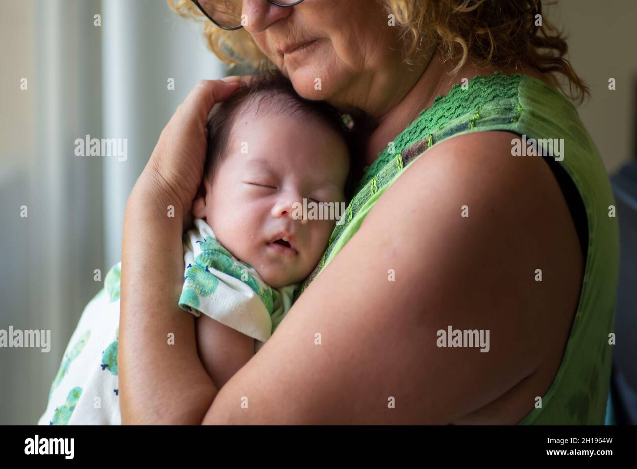 Grandmother holding sleeping 40 days old newborn baby boy by the window at home Stock Photo