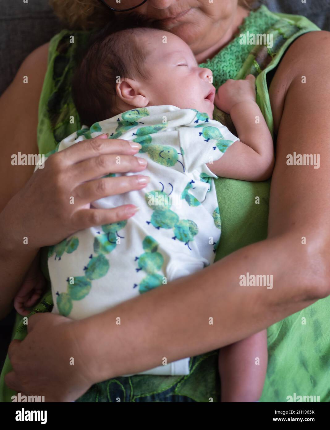 Grandmother holding sleeping 40 days old newborn baby boy on a sofa bed at home Stock Photo