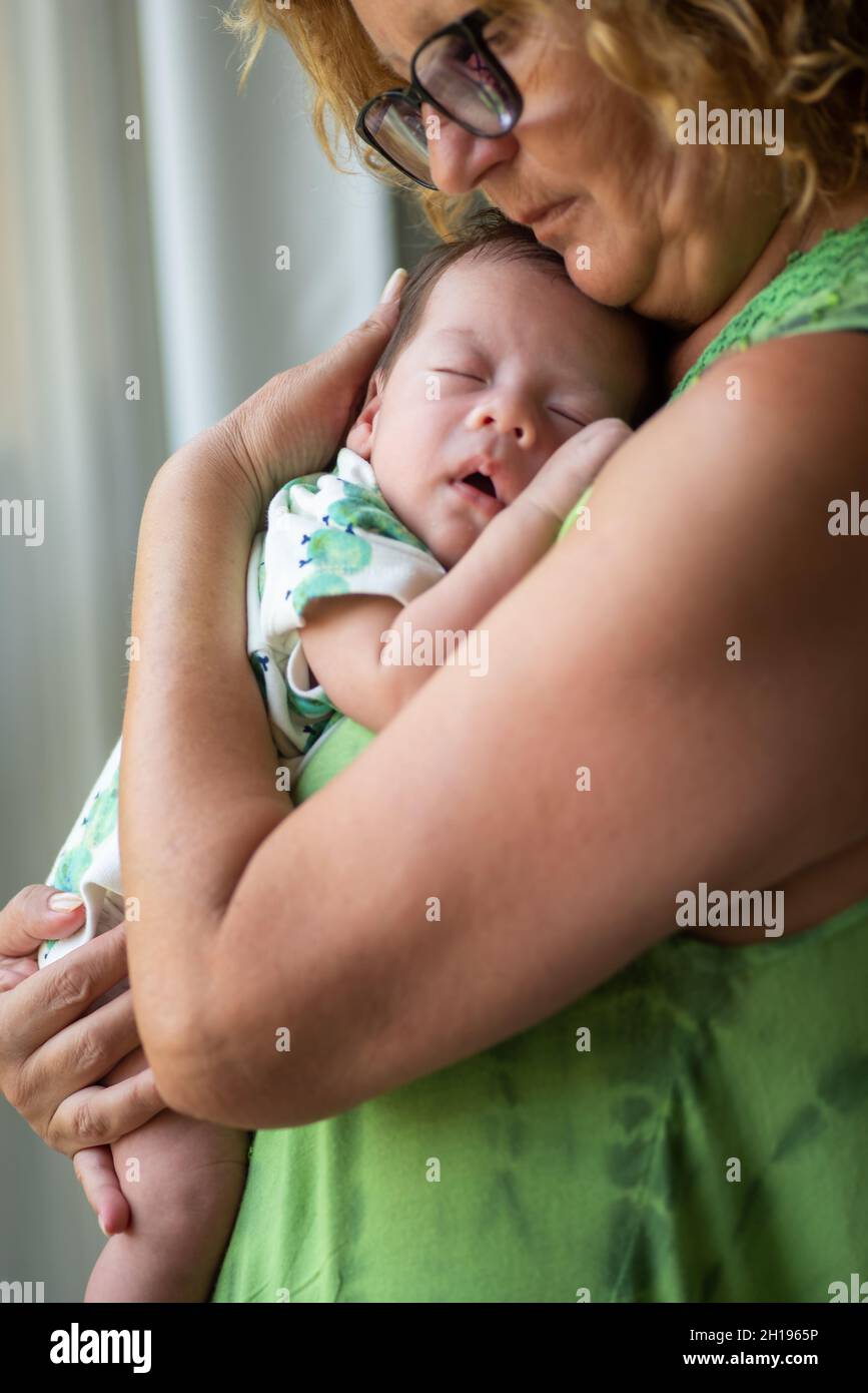 Grandmother holding sleeping 40 days old newborn baby boy by the window at home Stock Photo