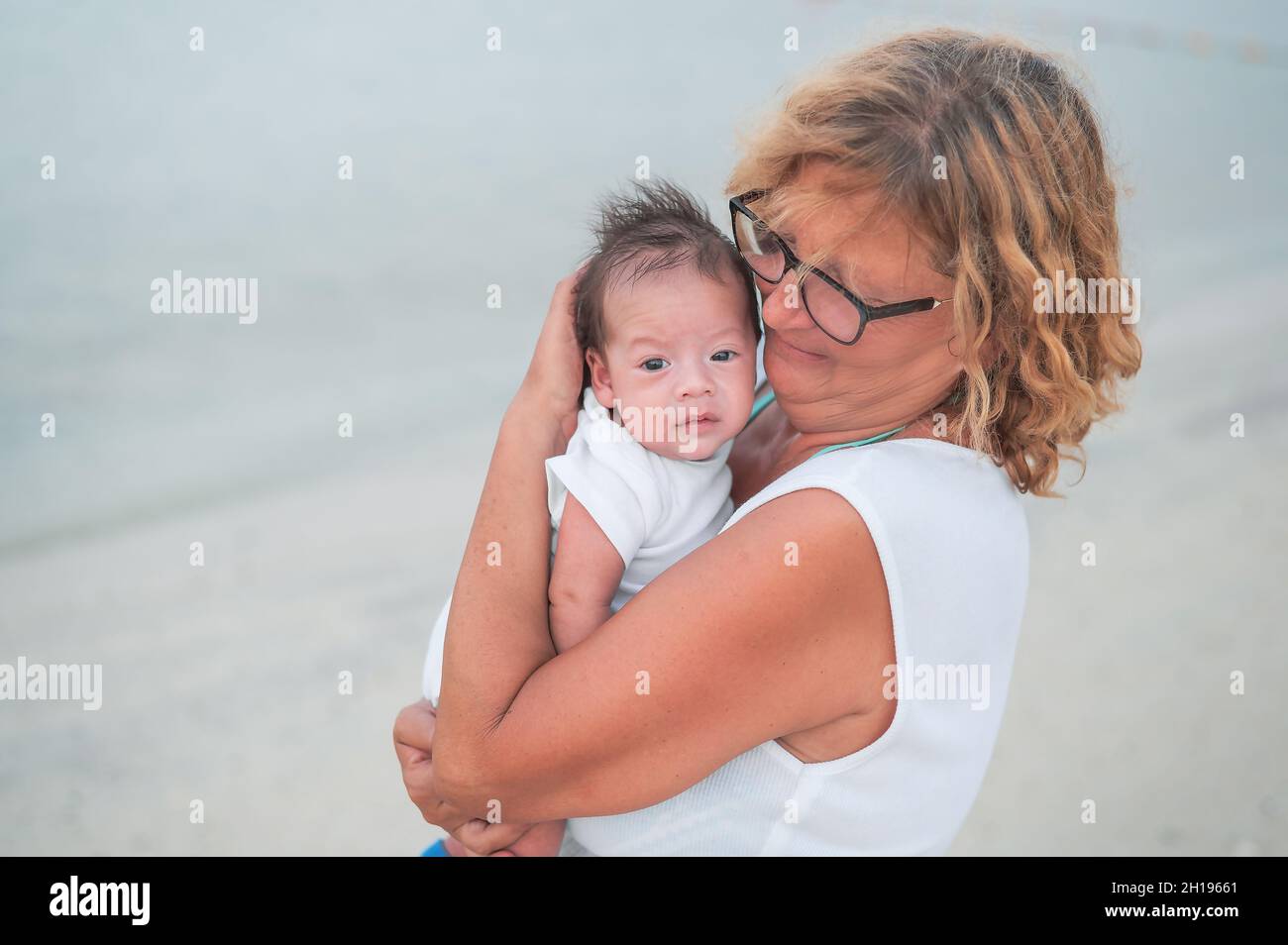 Grandma holding newborn baby boy at the beach by the seaside on the