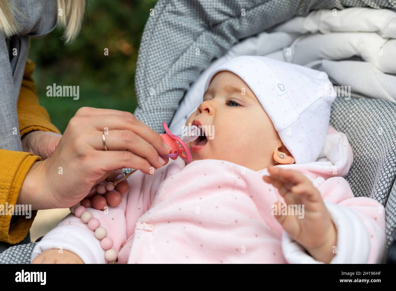 Baby girl with a pacifier in his mouth sitting in a stroller outdoor