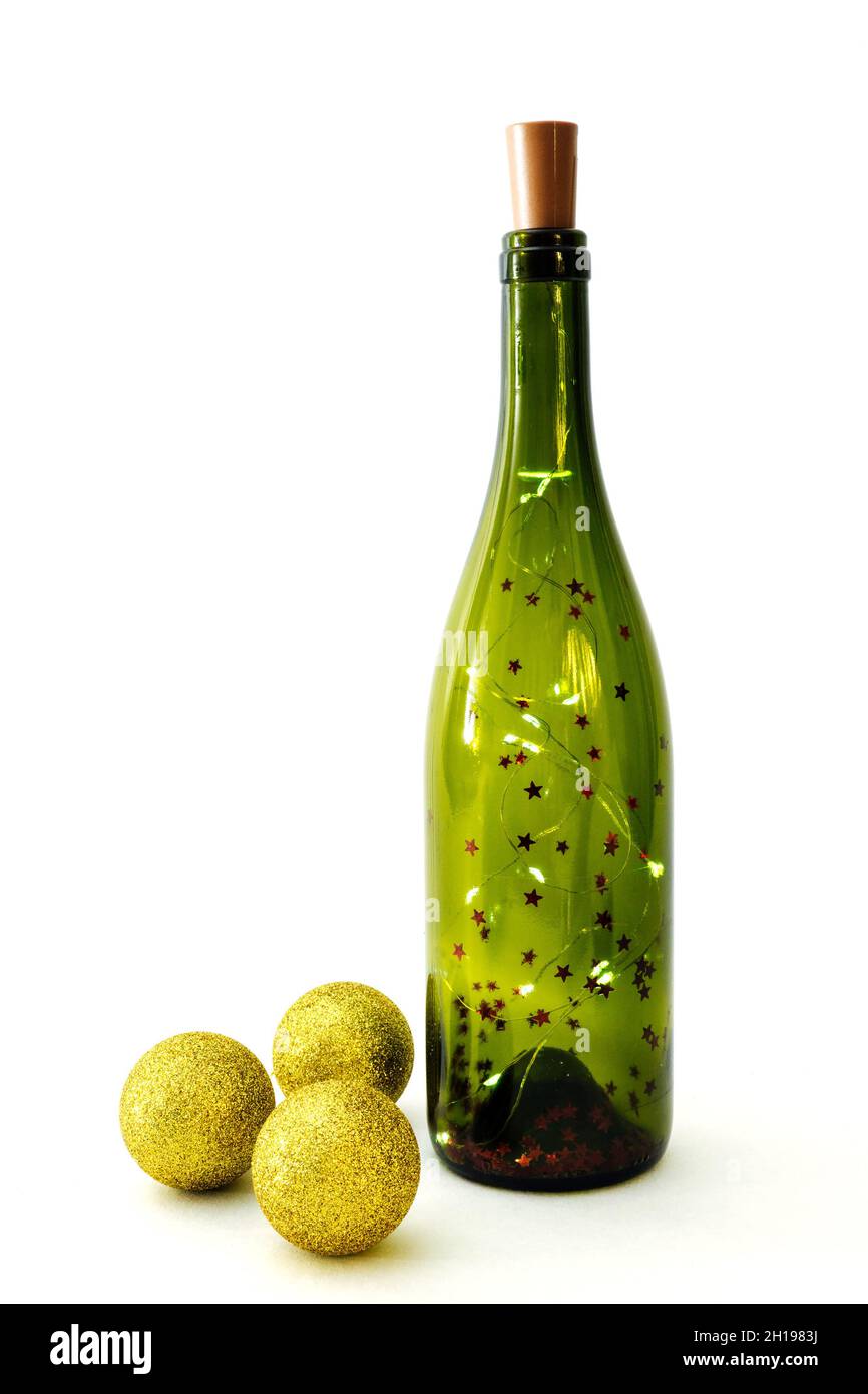 Garland in glass bottle for wine and three golden shiny christmas balls on white background. Selective focus, vertical view Stock Photo