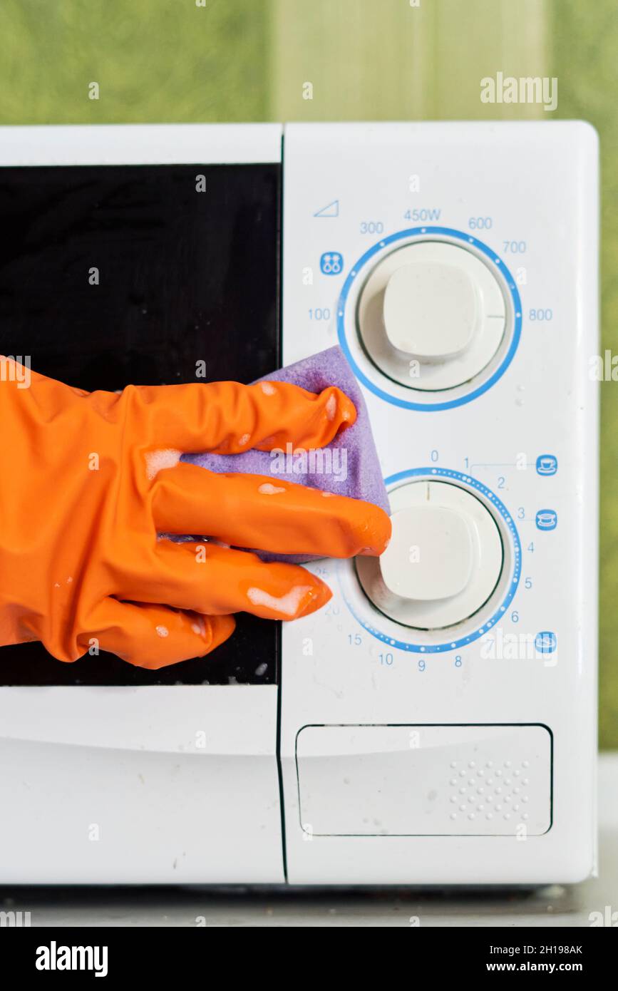 Woman in rubber gloves cleaning microwave oven with sponge in kitchen. Cleaning microwave in the kitchen Stock Photo