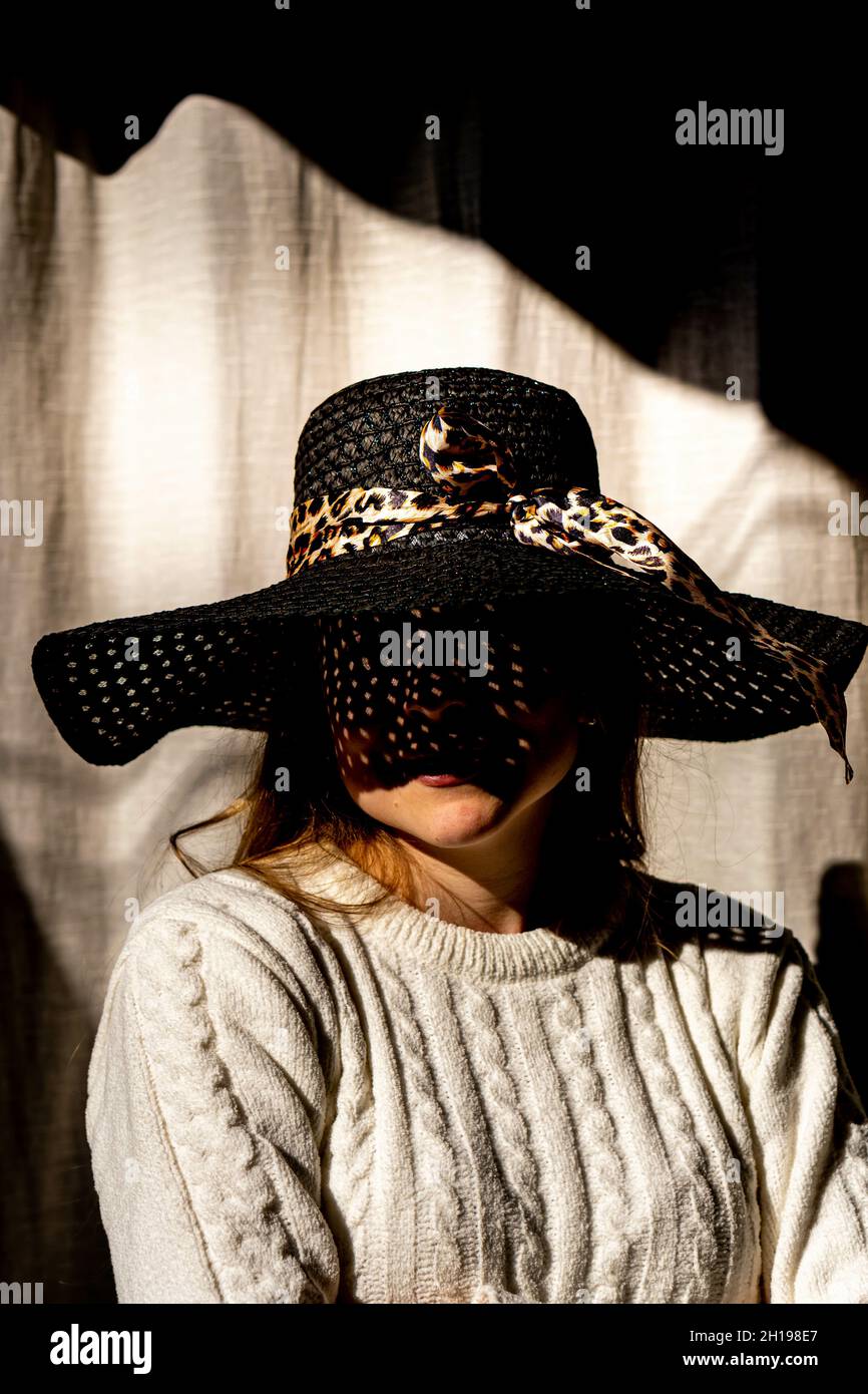 A portrait of a female wearing a black straw hat covering her face