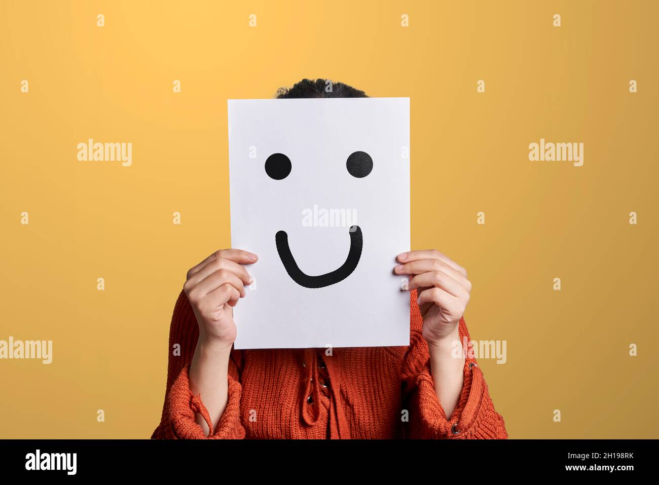 Woman holds a paper with drawn fake smile. Woman hiding her feelings and expressions, covering face with paper and fake good mood smile Stock Photo