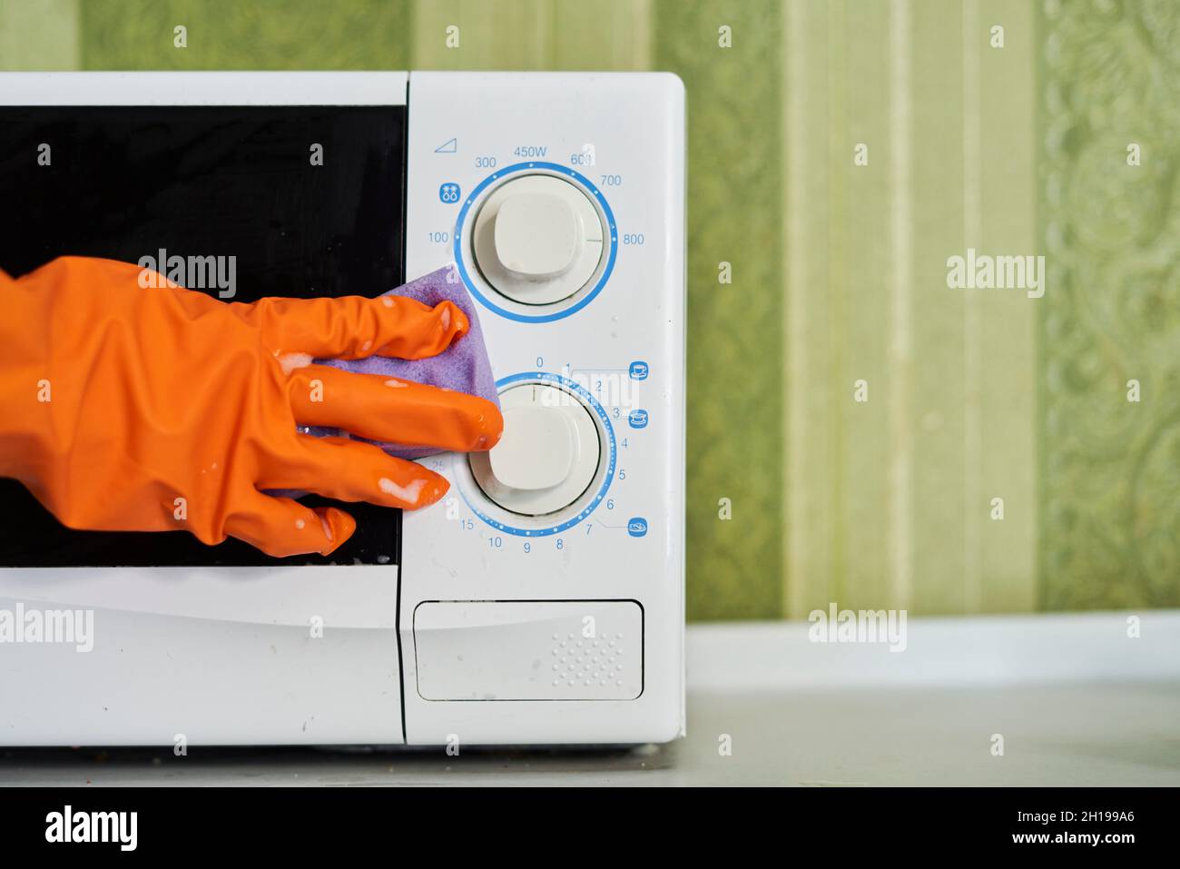 Woman in rubber gloves cleaning microwave oven with sponge in kitchen. Cleaning microwave in the kitchen Stock Photo