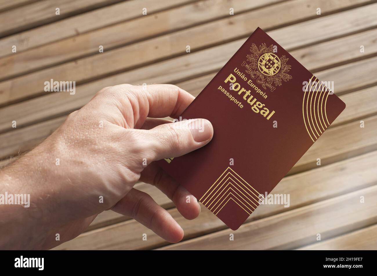 A hand holds a Portuguese passport and a wooden board in the background