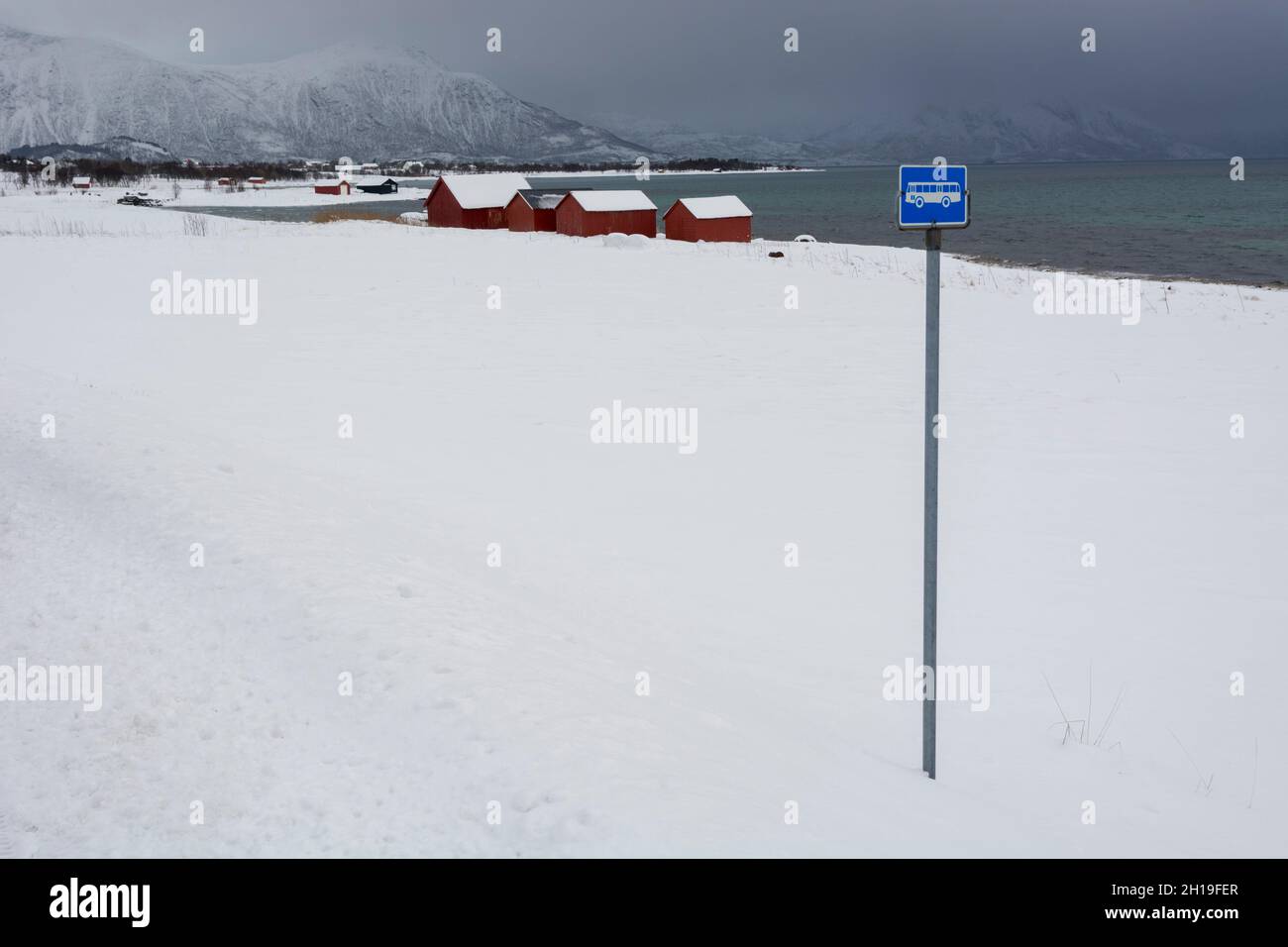 A bus stop and red houses by the sea in a snowy winter landscape ...