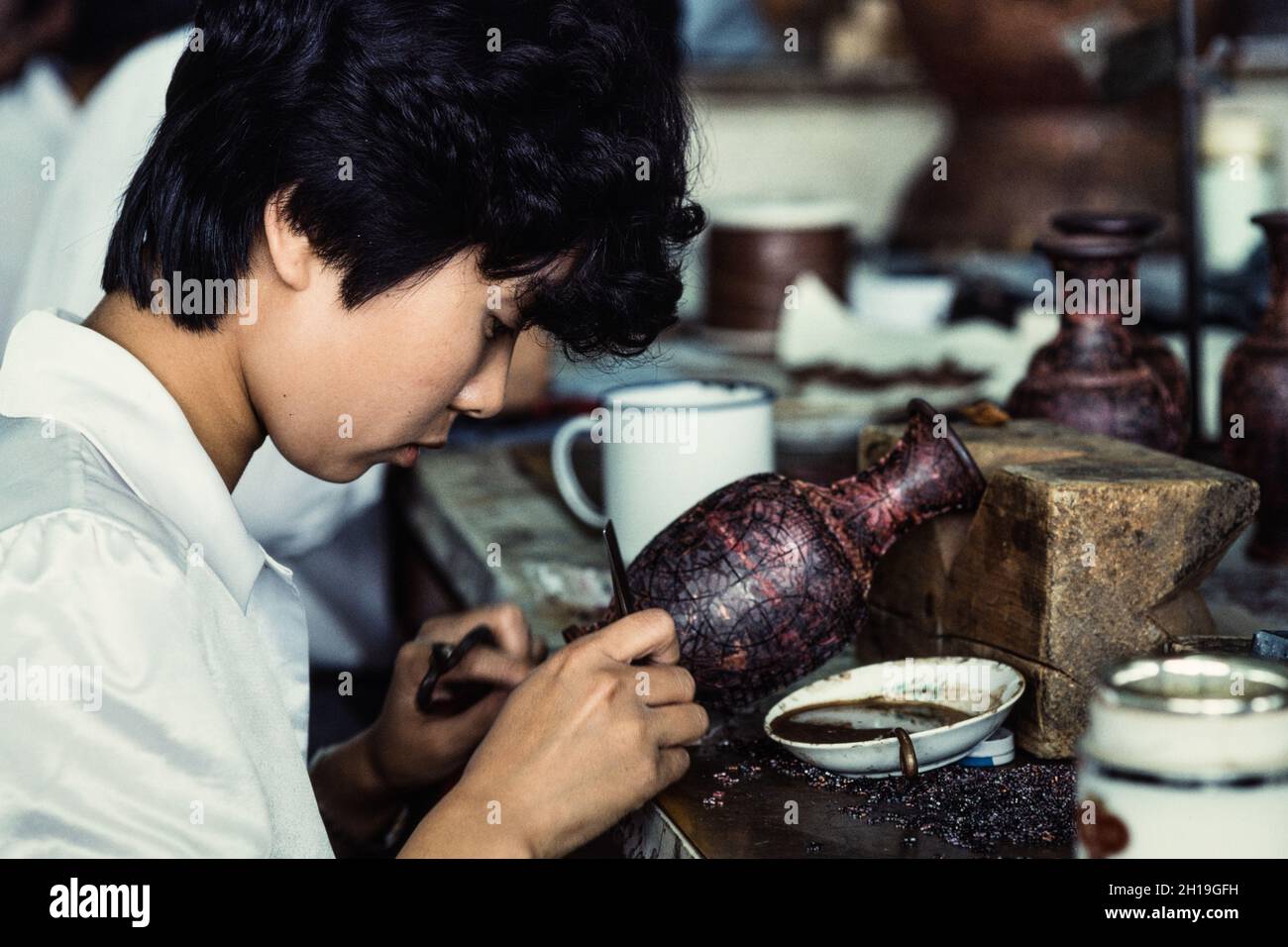 An artisan attaches cloisons or wire strip to make the design for a cloissone vase in a workshop in Beijing, China. Stock Photo
