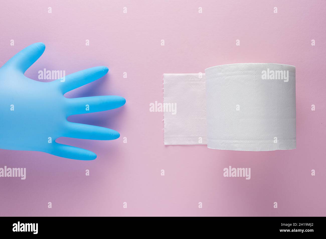Creative layout of toilet paper roll and medical glove on pink