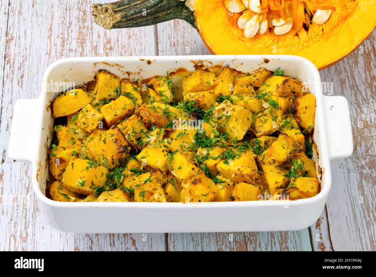 Roasted pumpkin in a ceramic pot on table with half raw squash Stock Photo Alamy