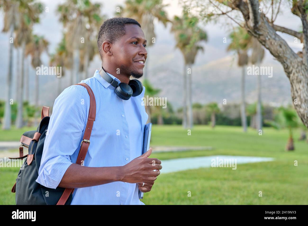 Outdoor portrait of young man with laptop headphones and backpack Stock Photo