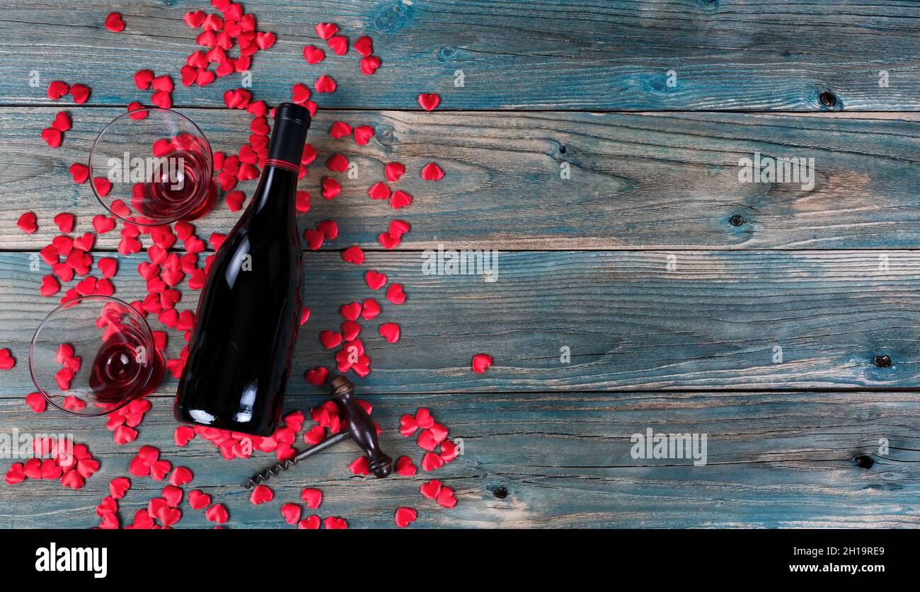 Valentines day holiday background with a bottle of wine, drinking glasses, corkscrew opener and little heart shapes on faded blue wooden planks Stock Photo