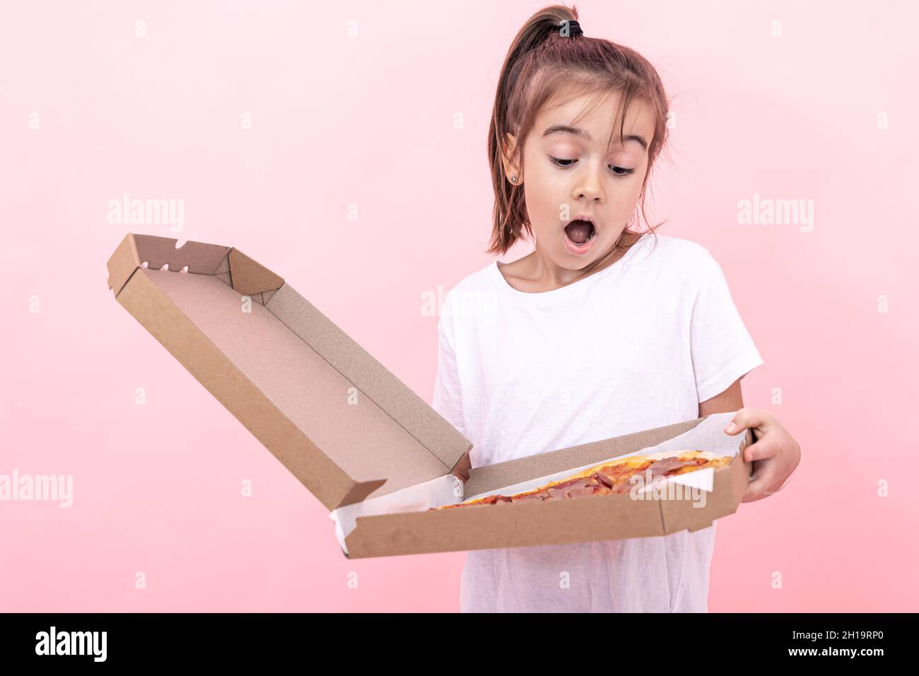 Funny little girl with pizza in a box on a pink background. Stock Photo
