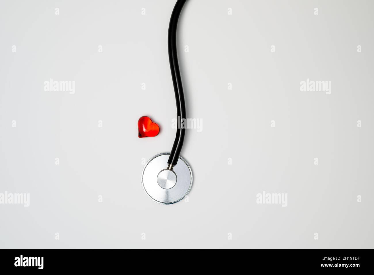 Health care or health check concept: red glass heart next to a medical stethoscope with chestpiece and tubing. Stock Photo