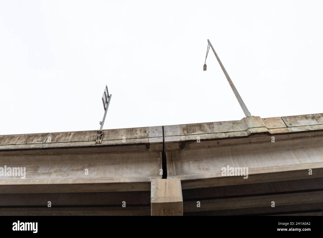 View looking up at the concrete supports of an elevated roadway bridge with light stanchion and sign post, horizontal aspect Stock Photo