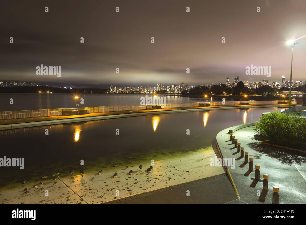 Night View of Kits Pool and Kitsilano Beach with Distant Vancouver, BC Canada City Lights Reflected of Cloudy Sky on Horizon Stock Photo