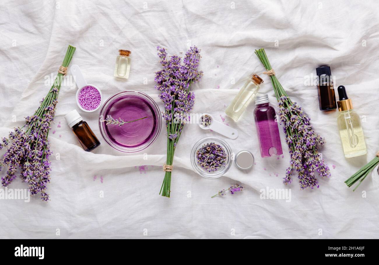 Lavender skincare cosmetics productsoils serum and lavender flowers on white fabric. Set natural spa beauty products. Lavender essential oil, serum Stock Photo