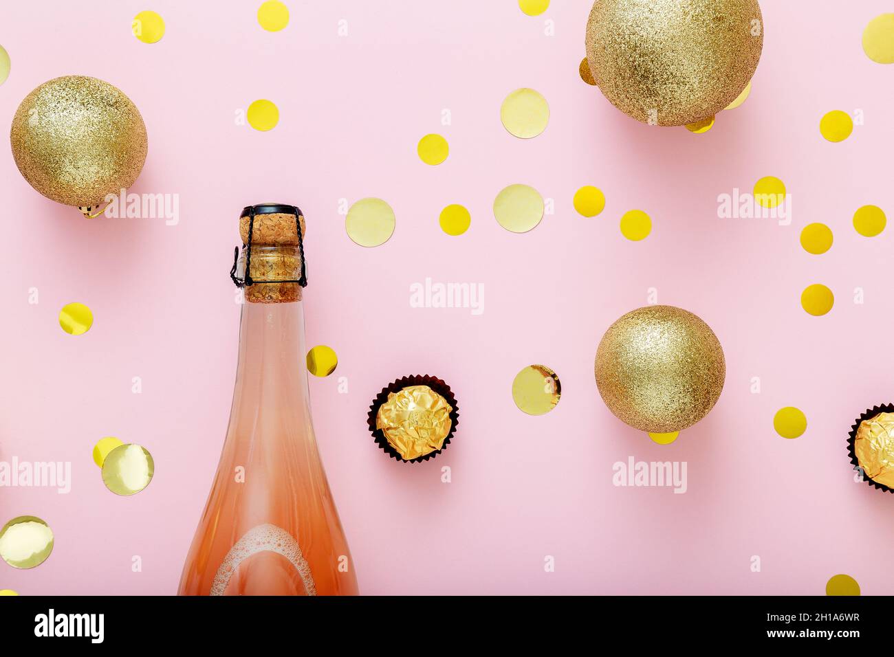 Pink champagne bottle with cork lid confetti and Christmas balls golden christmas decorations on pink background. Flat lay Close up Stock Photo