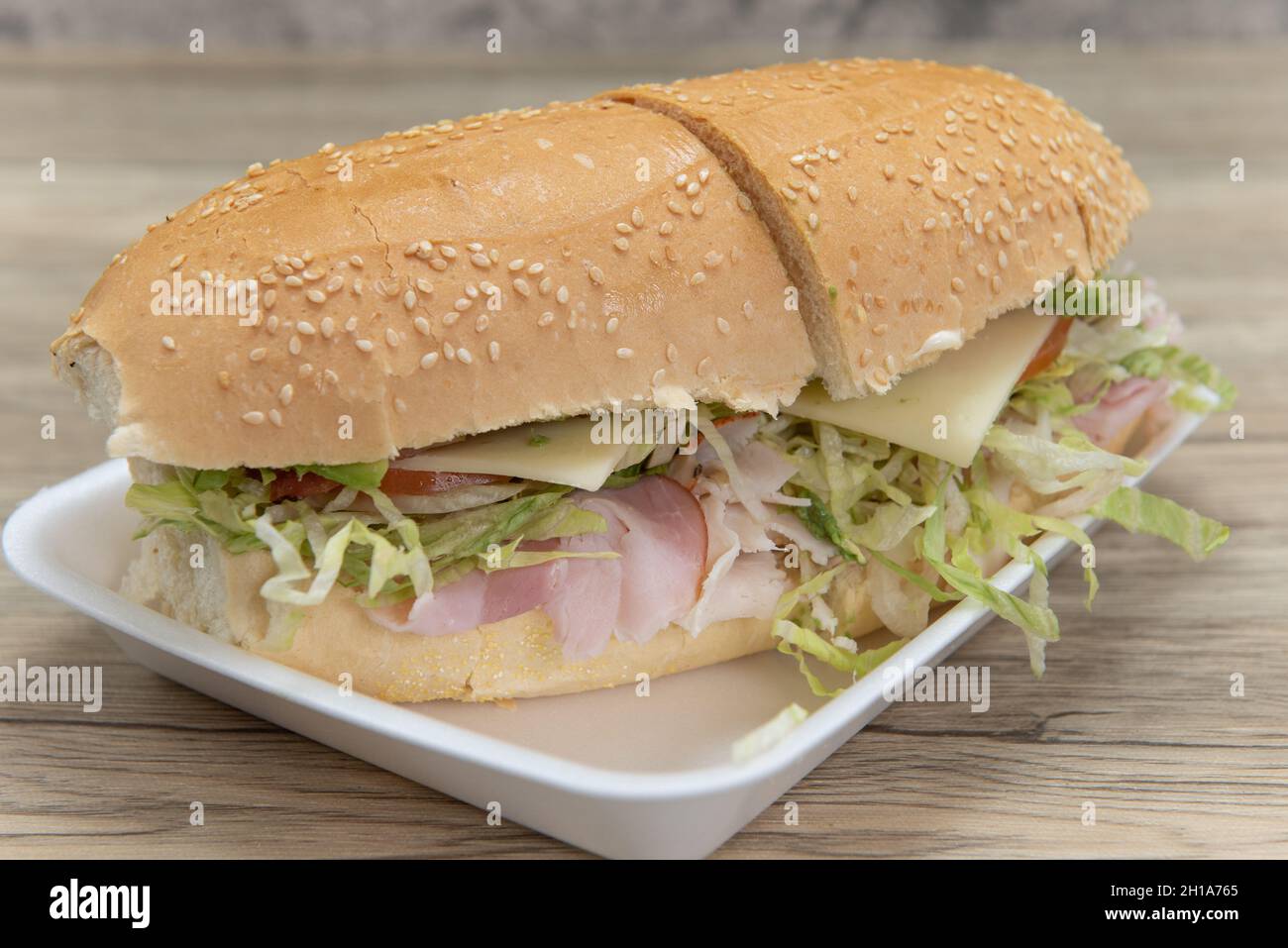 Handmade from fresh ingredients club sandwich with turkey, ham, swiss cheese, lettuce, bacon, and tomatoes, in a oven baked bun. Stock Photo