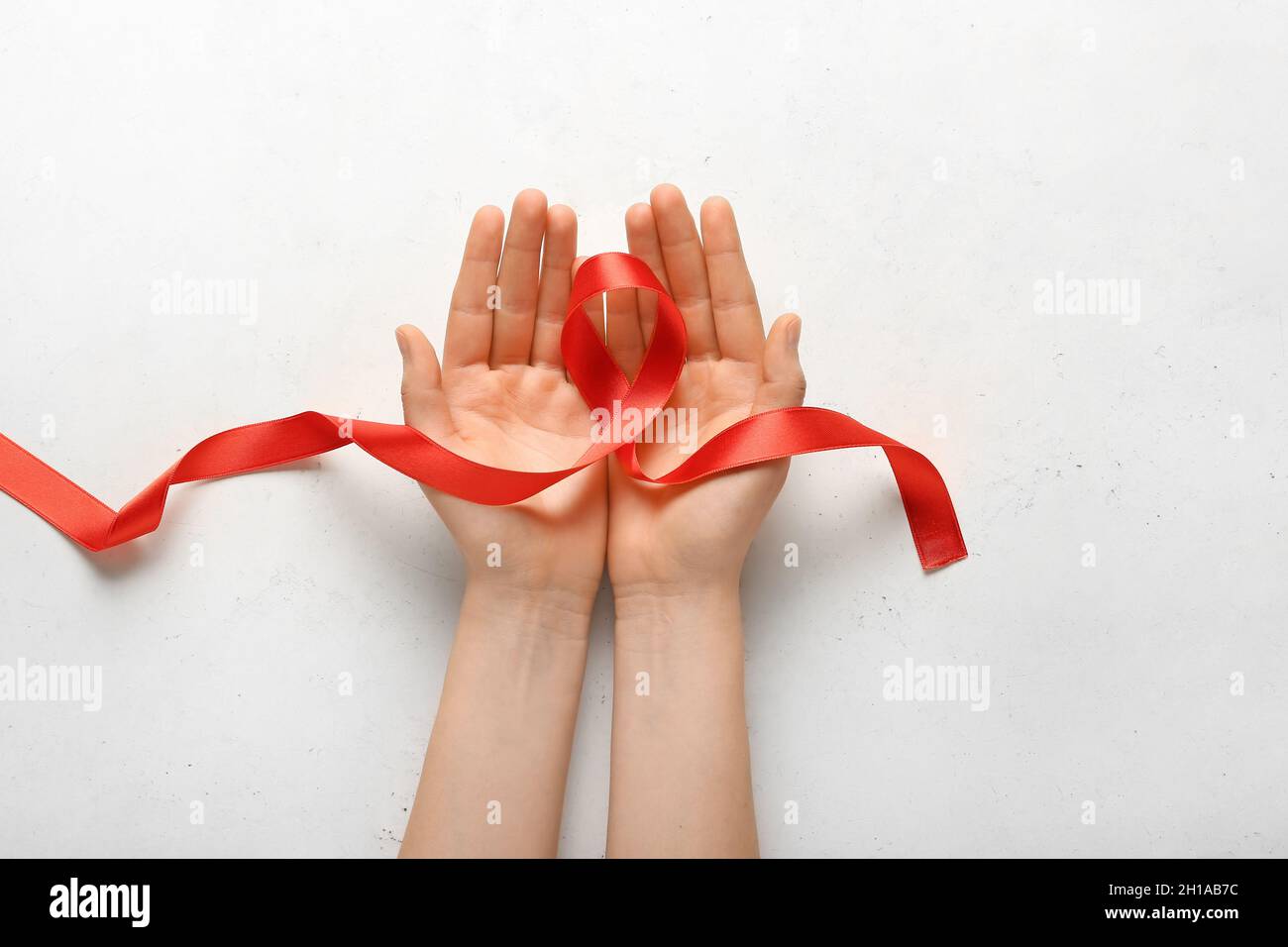 Female hands with red ribbon on light background Stock Photo - Alamy