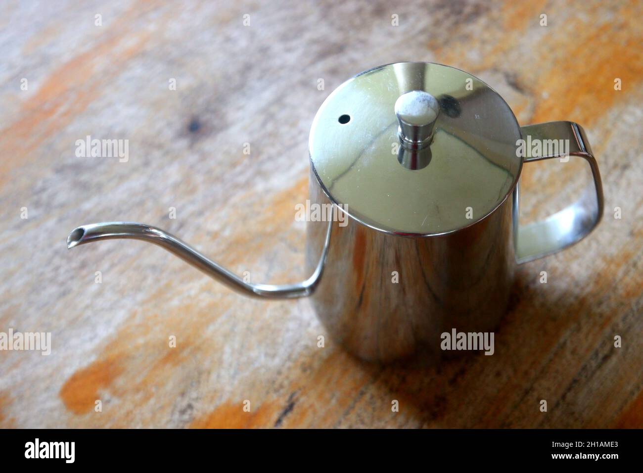 https://c8.alamy.com/comp/2H1AME3/stainless-steel-coffee-drip-kettle-jug-on-wooden-table-2H1AME3.jpg