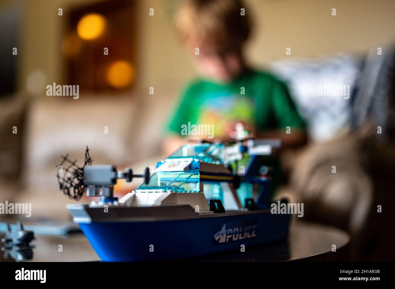 Tiffin, Iowa, USA - 9.2021 - Focus on Lego ship construction set with blurred child in the background playing Stock Photo