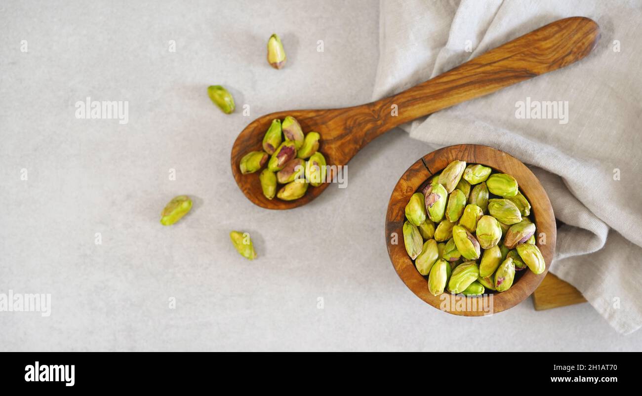 Pistachio nuts in a wooden rustic bowl and others pistachios on a wooden spoon top view overhead shot on light gray table on background banner with co Stock Photo