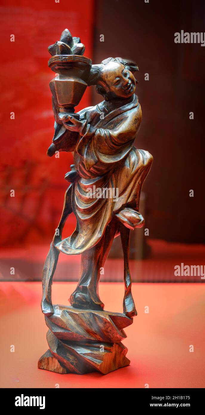 A 19th-century Chinese sculpture made of wood depicting a dancing Lan Caihe with a basket of flowers in his hands Stock Photo