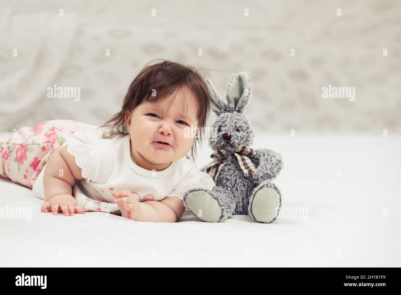 Crying six months old baby girl with a toy lying on blanket at home Stock Photo Alamy