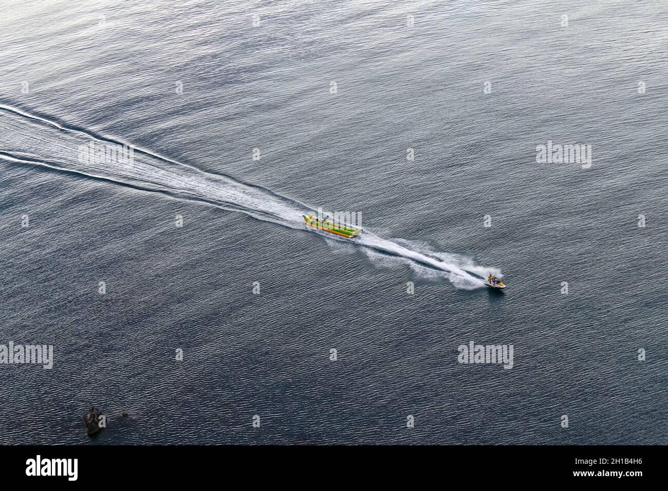 Jet ski towing an inflatable banana boat on the sea. Beautiful splashing. View from above. One of the activities at the seaside resort Stock Photo