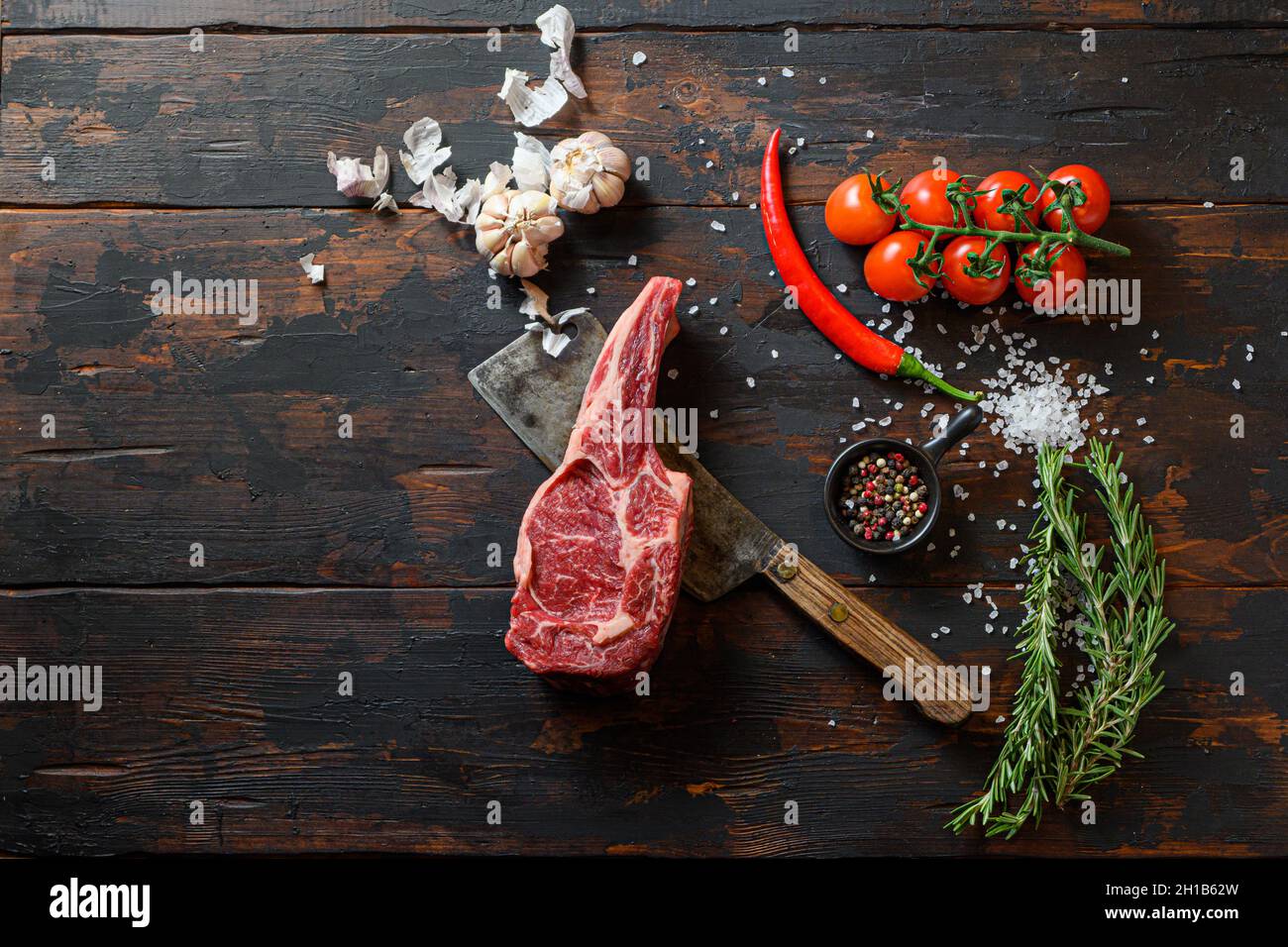 Raw Delmonico steak on meat cleaver. Organic farm marbled prime black angus beef. Dark wooden background. top view. With seasonings, peppercorns, chil Stock Photo