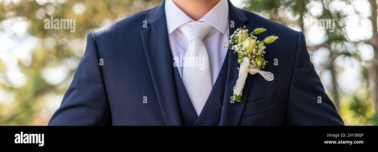 Unrecognizable young groom in elegant dark blue suit with beautiful white roses boutonniere. Groom fashion detail shot. Stock Photo