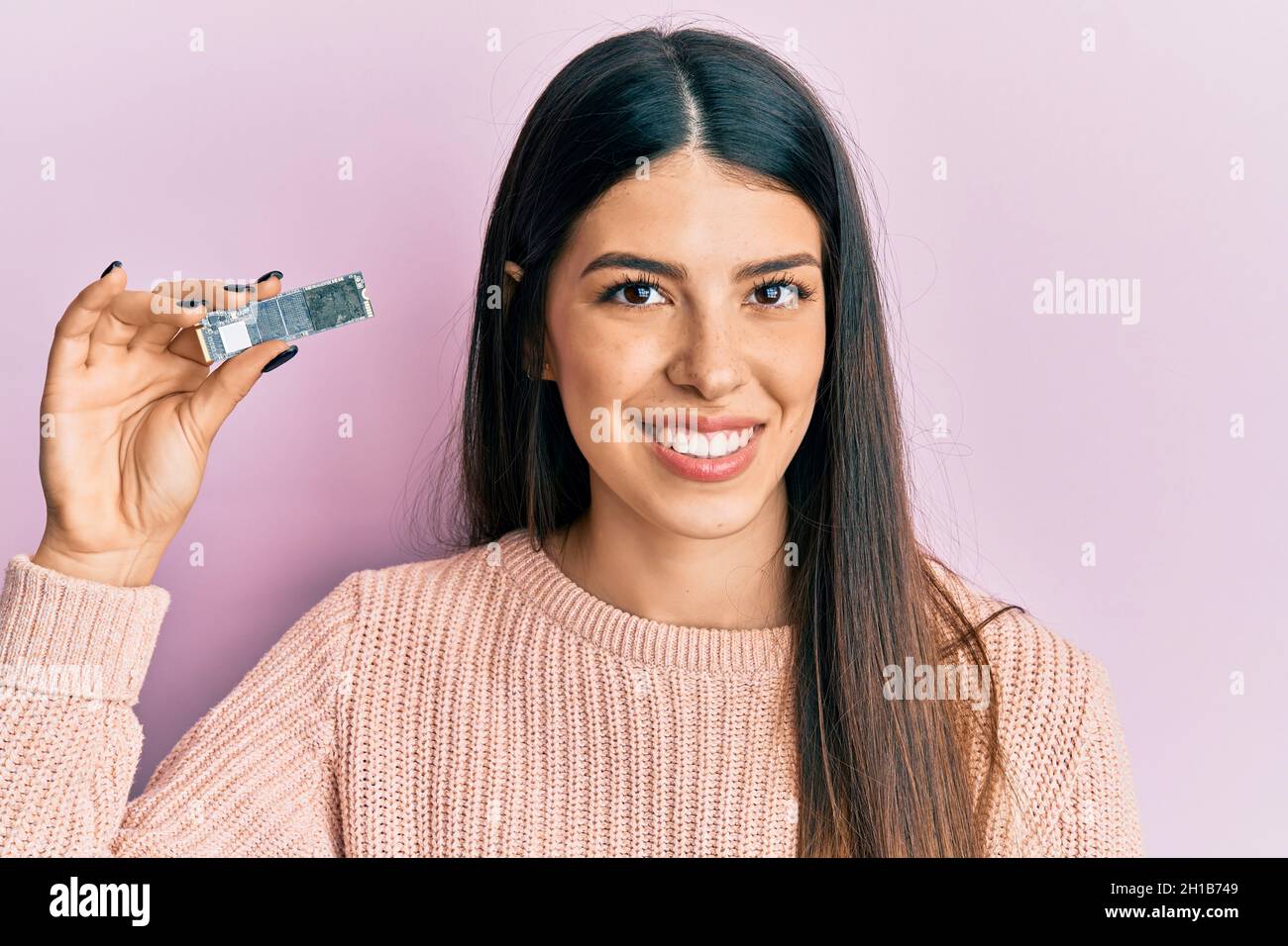 Young hispanic woman holding computer memory looking positive and happy standing and smiling with a confident smile showing teeth Stock Photo