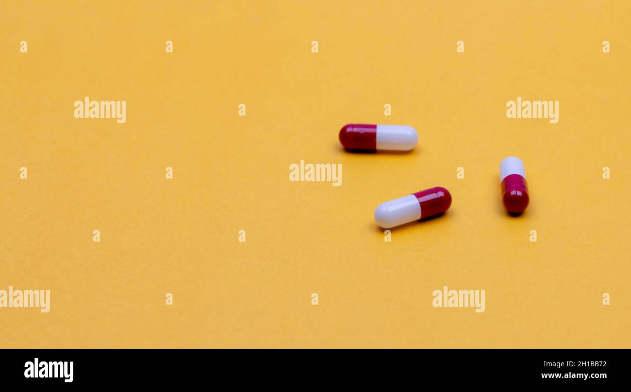 Red-white antibiotic capsule pills on yellow background. Prescription drug. Antibiotic drug resistance concept. Pharmaceutical industry. Pharmaceutics Stock Photo