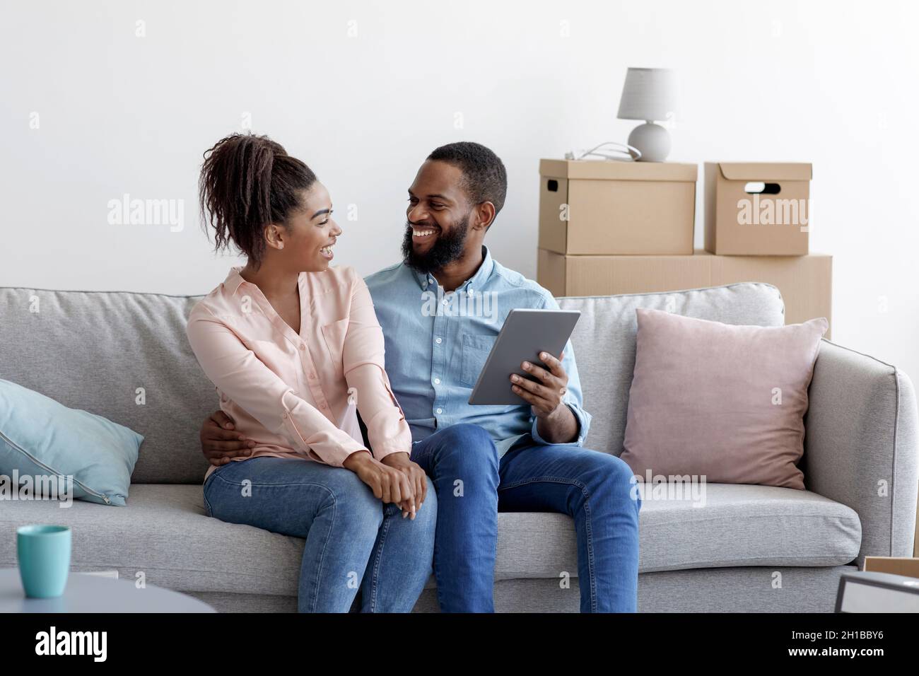 Happy young black male and female relax on couch using tablet for online buying furniture Stock Photo