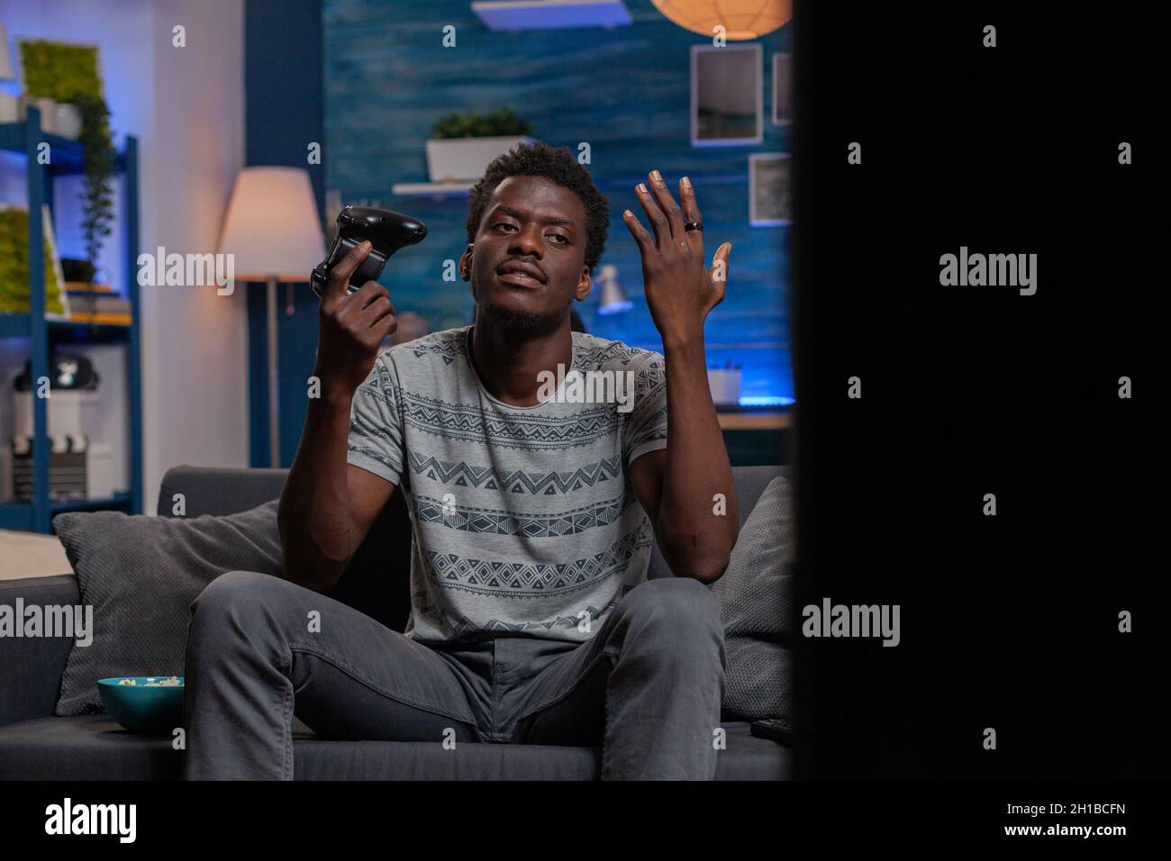 African american player losing online videogames during virtual gaming competition sitting on couch in living room. Black gamer guy playing games using joystick enjoying free time Stock Photo