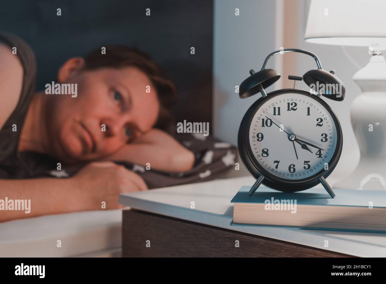 Sleepless insomniac woman lying in bed and looking at alarm clock on bedside nightstand, selective focus Stock Photo