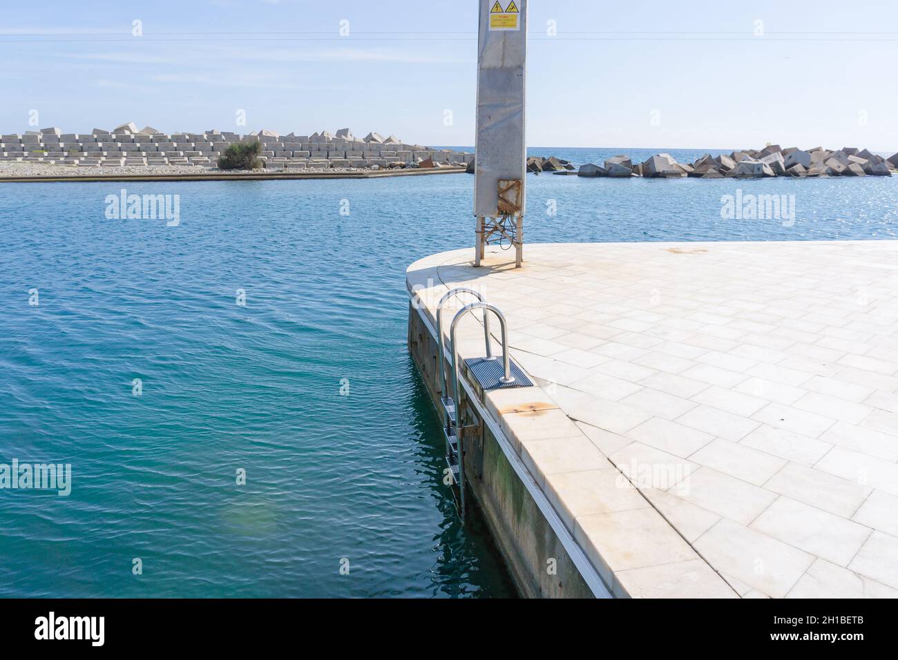 BARCELONA, SPAIN - OCTOBER 2, 2021: Pool ladder on a white marble pier in front of a sign forbidden to climb the tower due to danger of electrocution Stock Photo