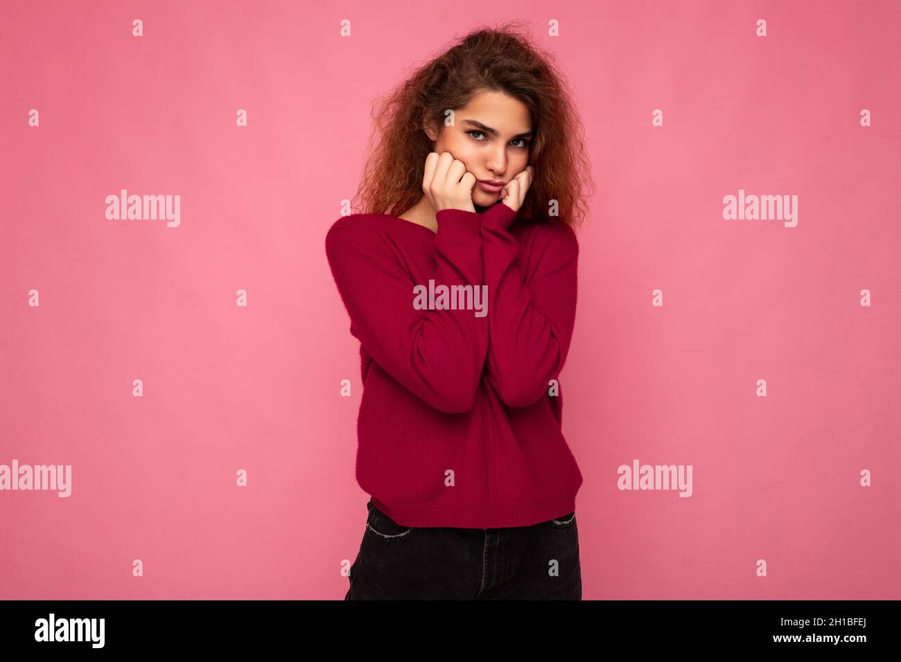 Portrait of young emotional offended touchy beautiful brunette curly woman with sincere emotions wearing trendy pink pullover isolated on pink Stock Photo