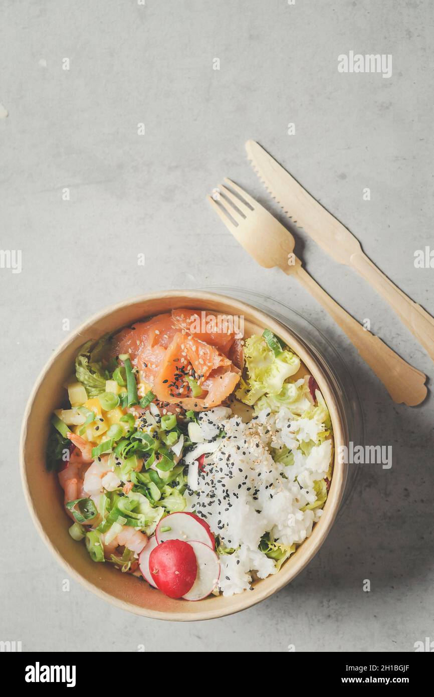 Modern sustainable food delivery with eco friendly packaging and cutlery. Healthy Asian take away food : salad bowl with salmon on grey concrete kitch Stock Photo