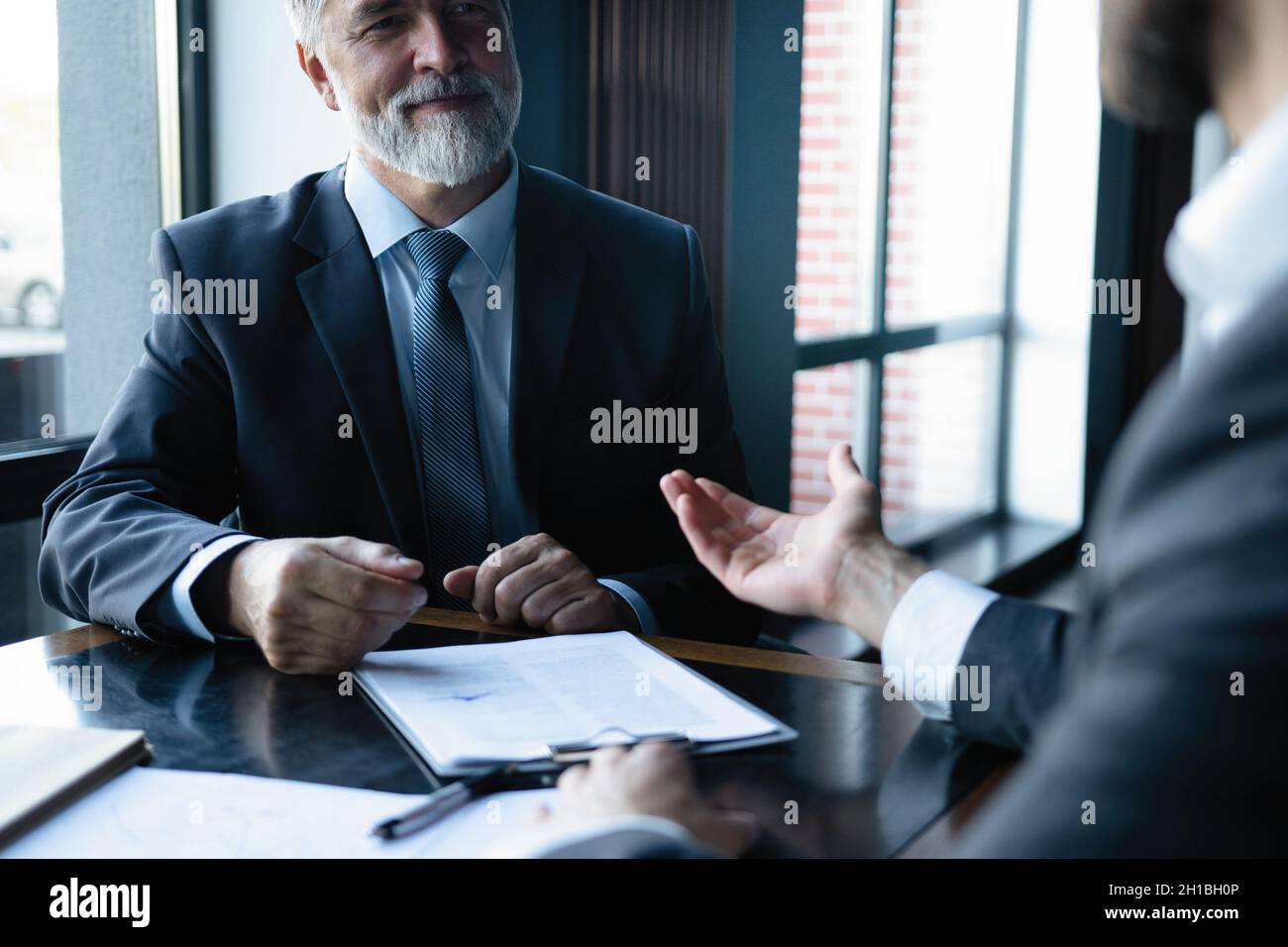 Senior and junior businessman discuss something during their meeting, office background. Stock Photo