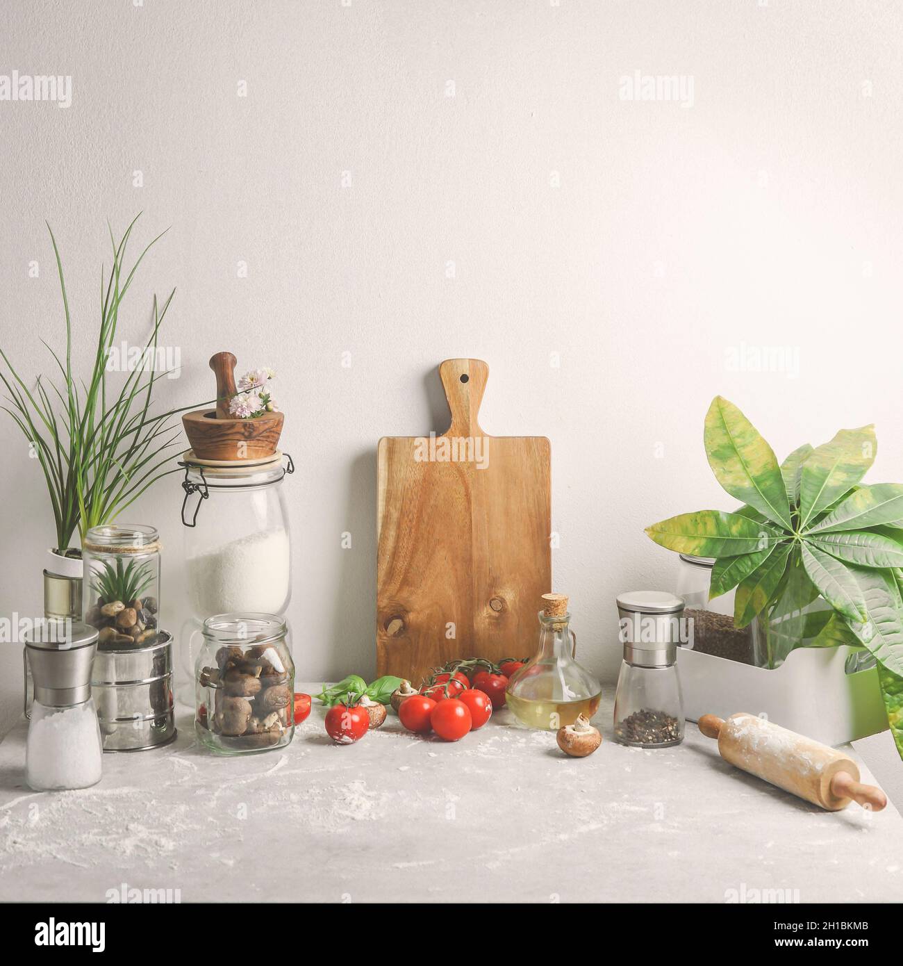 Waste-free domestic kitchen still life background with glass jars, wooden cutting board, plants, glass utensils, mortar and pestle on pale grey table Stock Photo