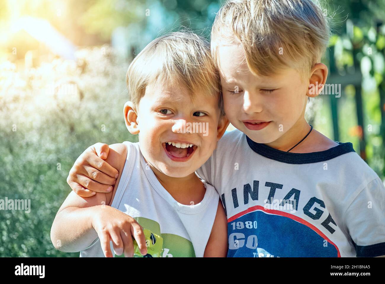 Little Boy Hugs Happy Junior Brother With Small Toy Car Sitting On 