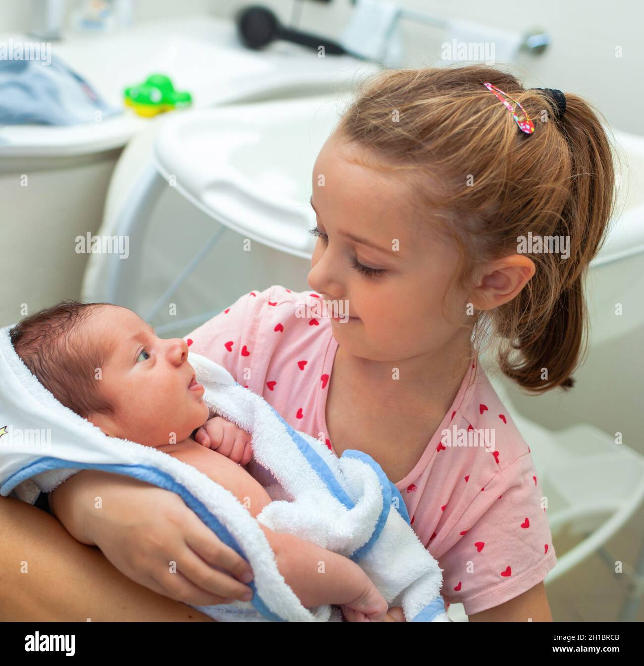 First bath of newborn baby boy. The baby is in the bathrobe in the arms of his little sister. Stock Photo