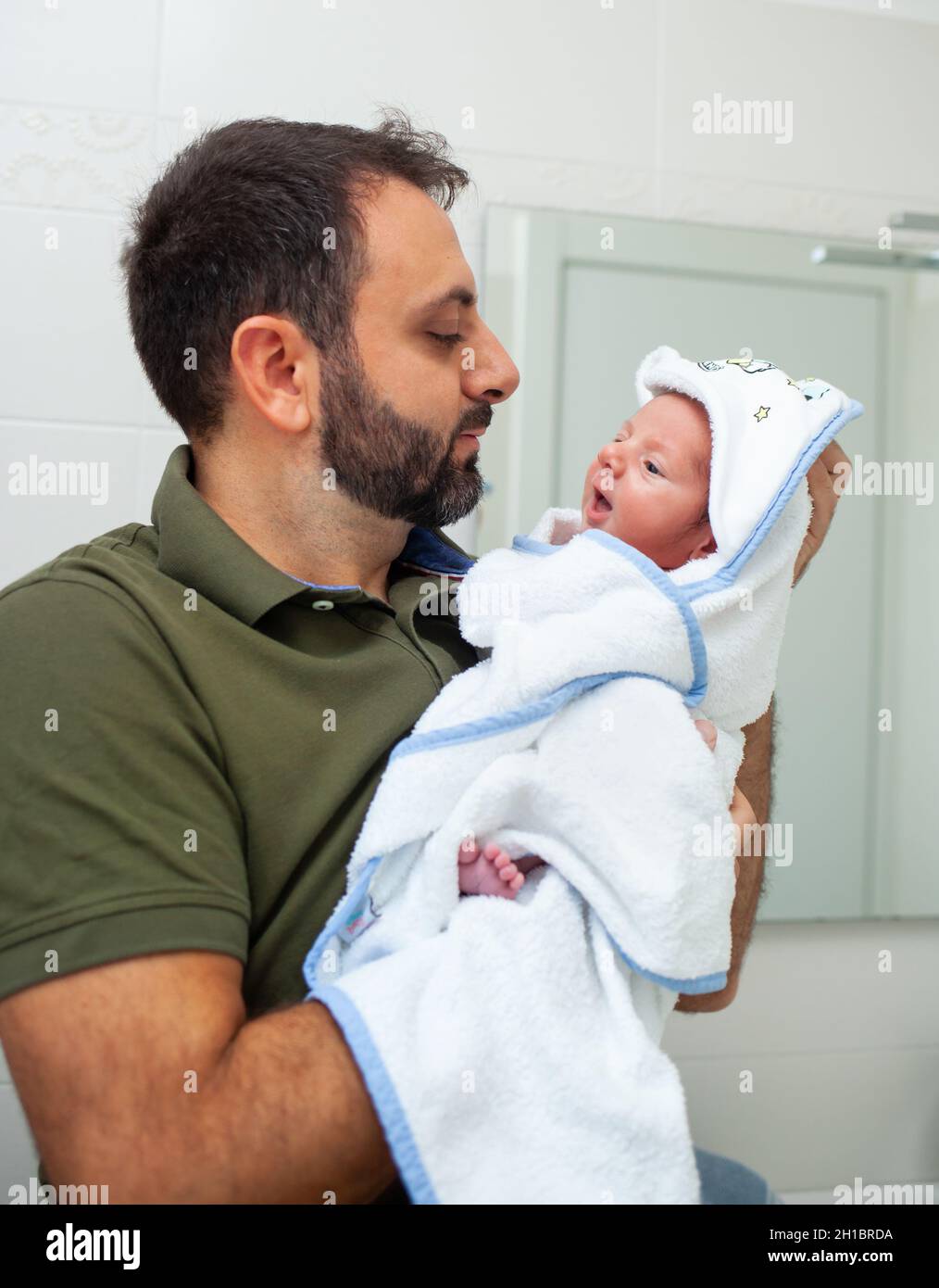 First bath of newborn baby boy. The baby is in the bathrobe in his father's arms. Stock Photo