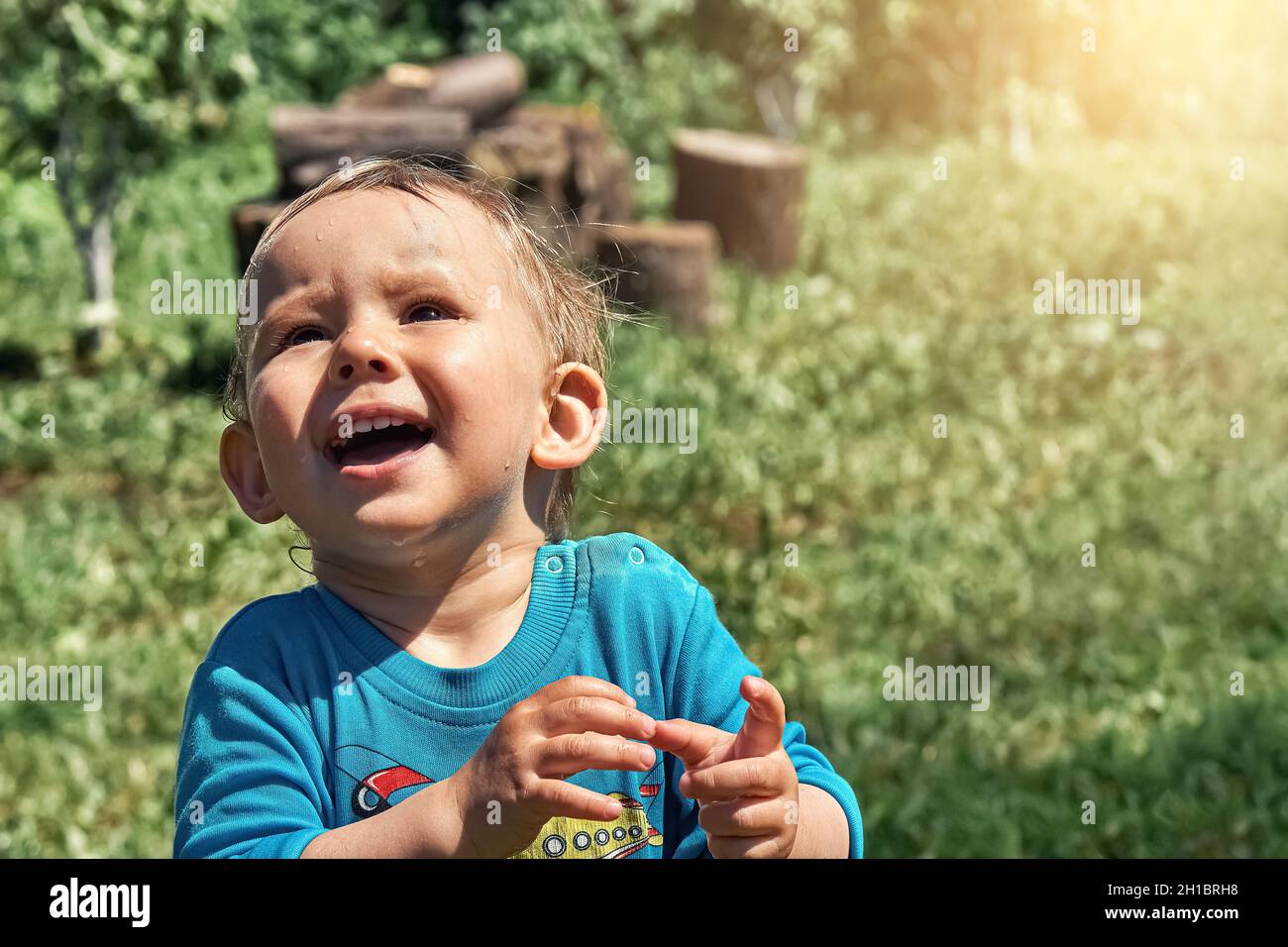 Funny toddler stares with deep admiration at flying bug on green field in yard of country house on sunny summer day closeup Stock Photo