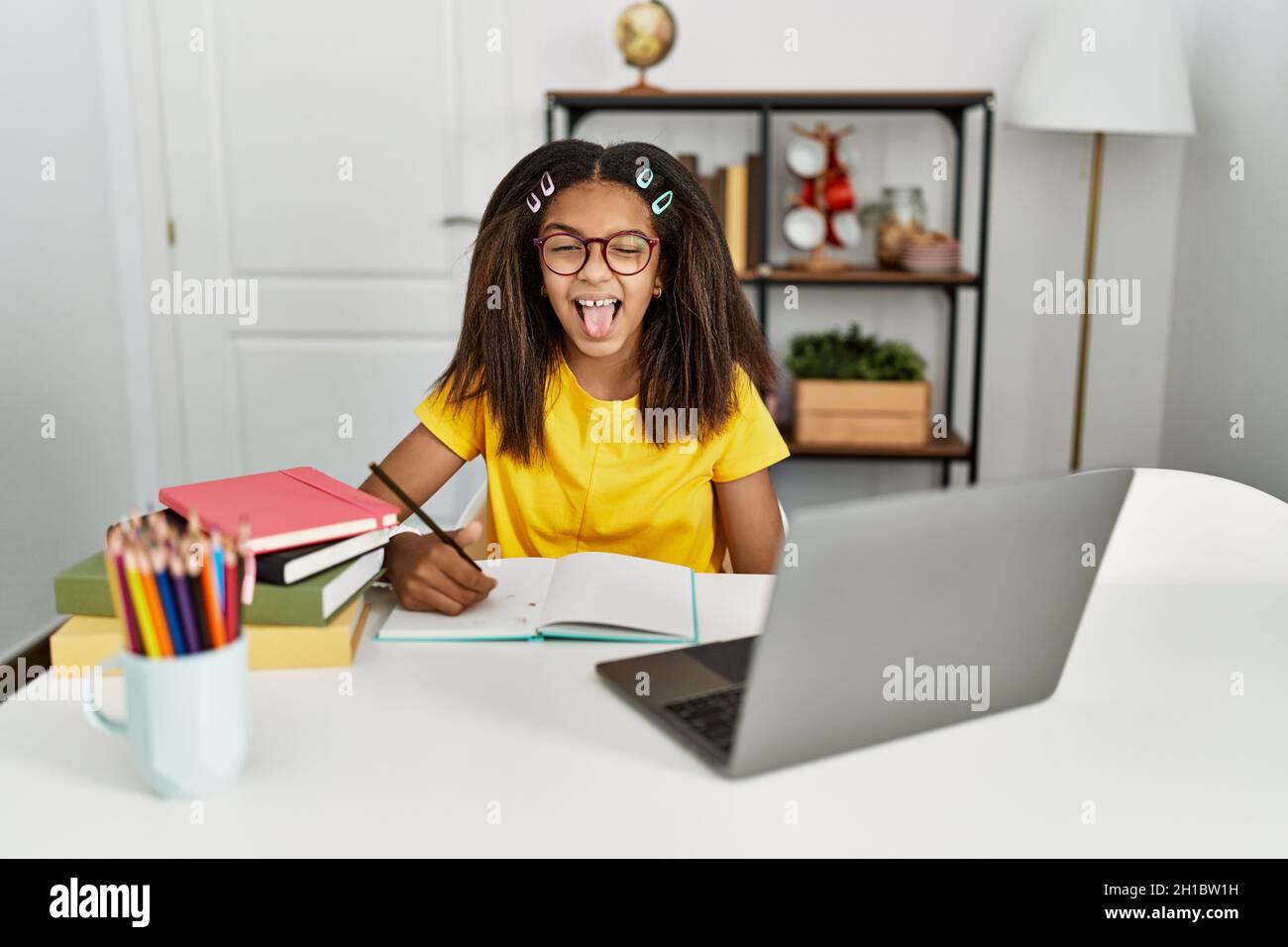 Young african american girl doing homework at home sticking tongue out ...