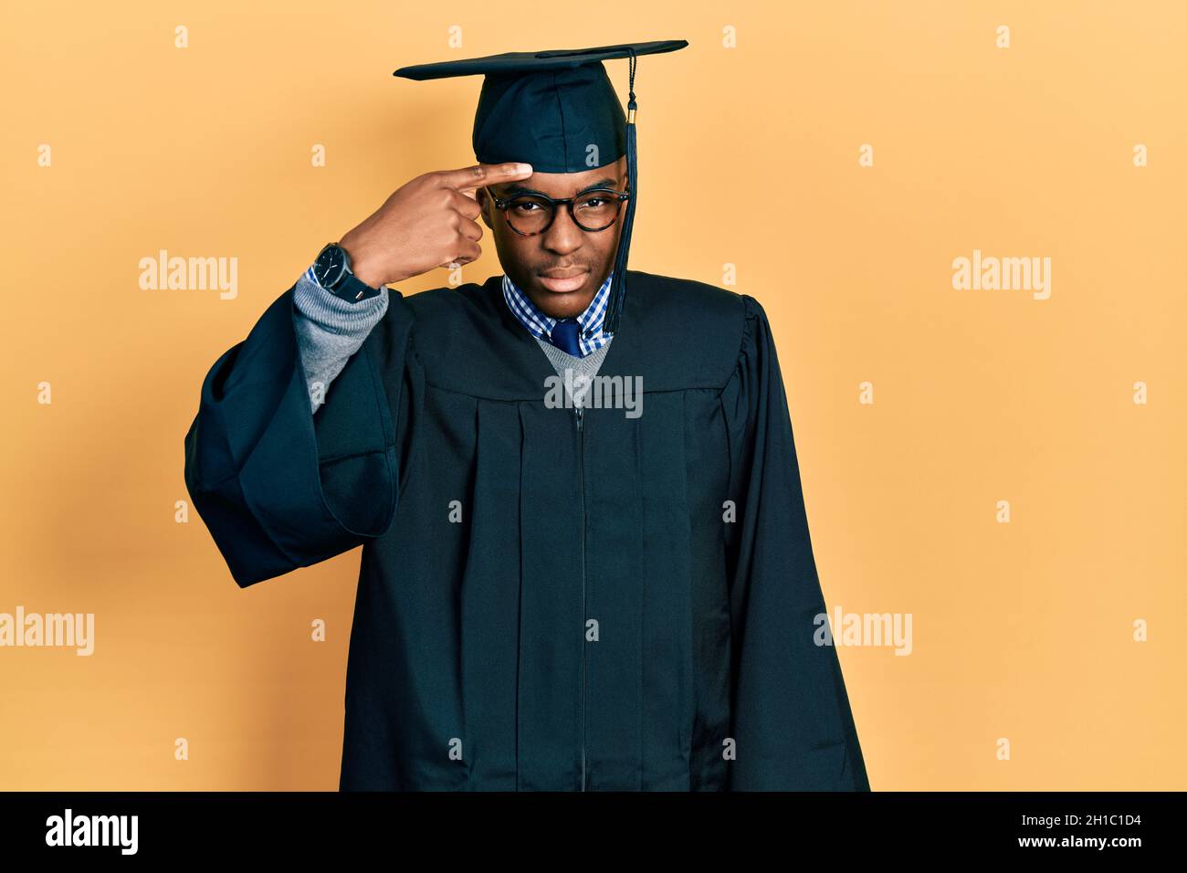 Young african american man wearing graduation cap and ceremony robe pointing unhappy to pimple on forehead, ugly infection of blackhead. acne and skin Stock Photo